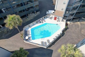 Eine Vogelperspektive zeigt ein Hotel mit Schwimmbad, Liegestühlen und einer kleinen Sonnenterrasse.