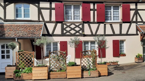 A traditional half-timbered building with red shutters, wooden lattice gates, and potted plants. - Gîte Le Colombage, 2 bedrooms, free parking, 25 km from Strasbourg (Scharrachbergheim)
