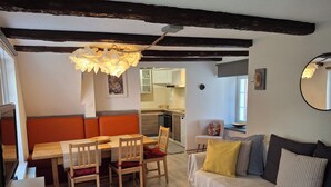 A cozy living room with a wooden dining table, orange cushioned bench, and a sofa with striped pillows. - Gîte Le Colombage, 2 bedrooms, free parking, 25 km from Strasbourg (Scharrachbergheim)