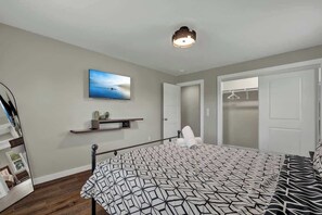Une chambre à coucher comprenant un lit, une table de chevet, un téléviseur fixé au mur, un luminaire au plafond et une porte donnant sur un placard.
