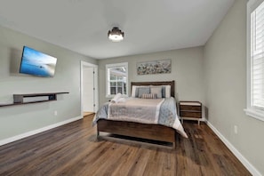 A bedroom with a bed, a TV mounted on the wall, and a window with blinds.
