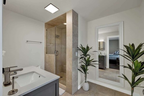 A modern bathroom with a large sink, a shower with glass doors, and two potted plants.