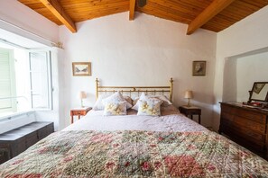 A bedroom with a wooden ceiling, a bed with floral pillows, two bedside tables with lamps, and a dresser. - Cozy Cottage Retreat in Bajardo (Bajardo)