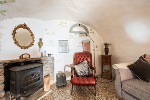 Um quarto aconchegante com lareira de pedra, uma poltrona de couro vermelha, uma mesa pequena com abajur e um quadro na parede.