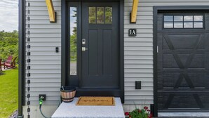 Une porte d’entrée noire avec une boîte aux lettres, un paillasson et un petit jardin agrémenté de fleurs rouges.