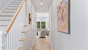 Un couloir avec un escalier en bois, des murs blancs et un parquet clair.