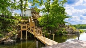 A wooden dock leading to a house surrounded by lush greenery and a calm body of water. - Lakefront Luxury Retreat, Kayaks, Game Room, Firepit, Pool Table & Private Dock (Wedowee)