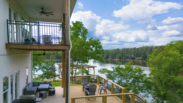 A two-story building with a balcony overlooking a lake, outdoor seating, and a pergola. - Lakefront Luxury Retreat, Kayaks, Game Room, Firepit, Pool Table & Private Dock (Wedowee)