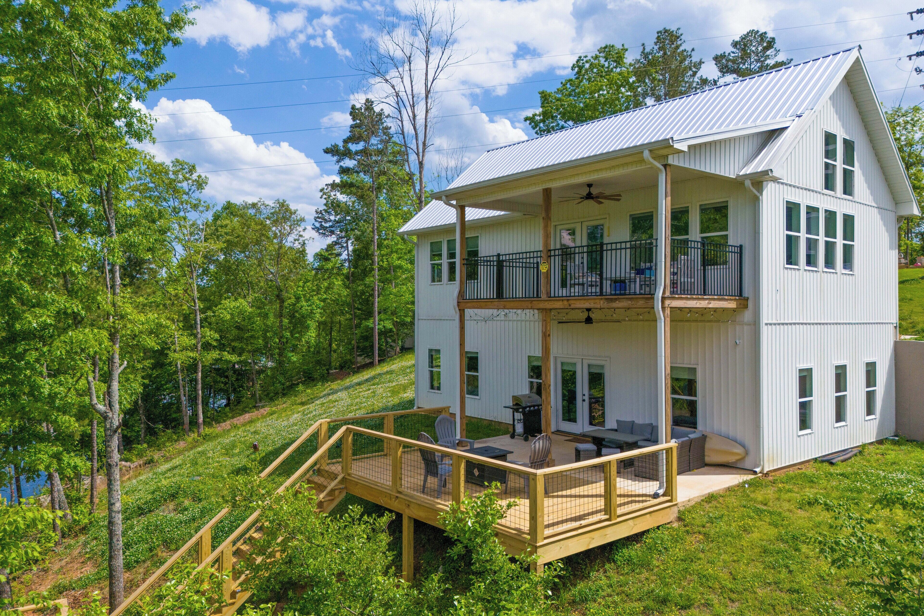 A two-story house with a balcony, a deck, and a view of a forested area.