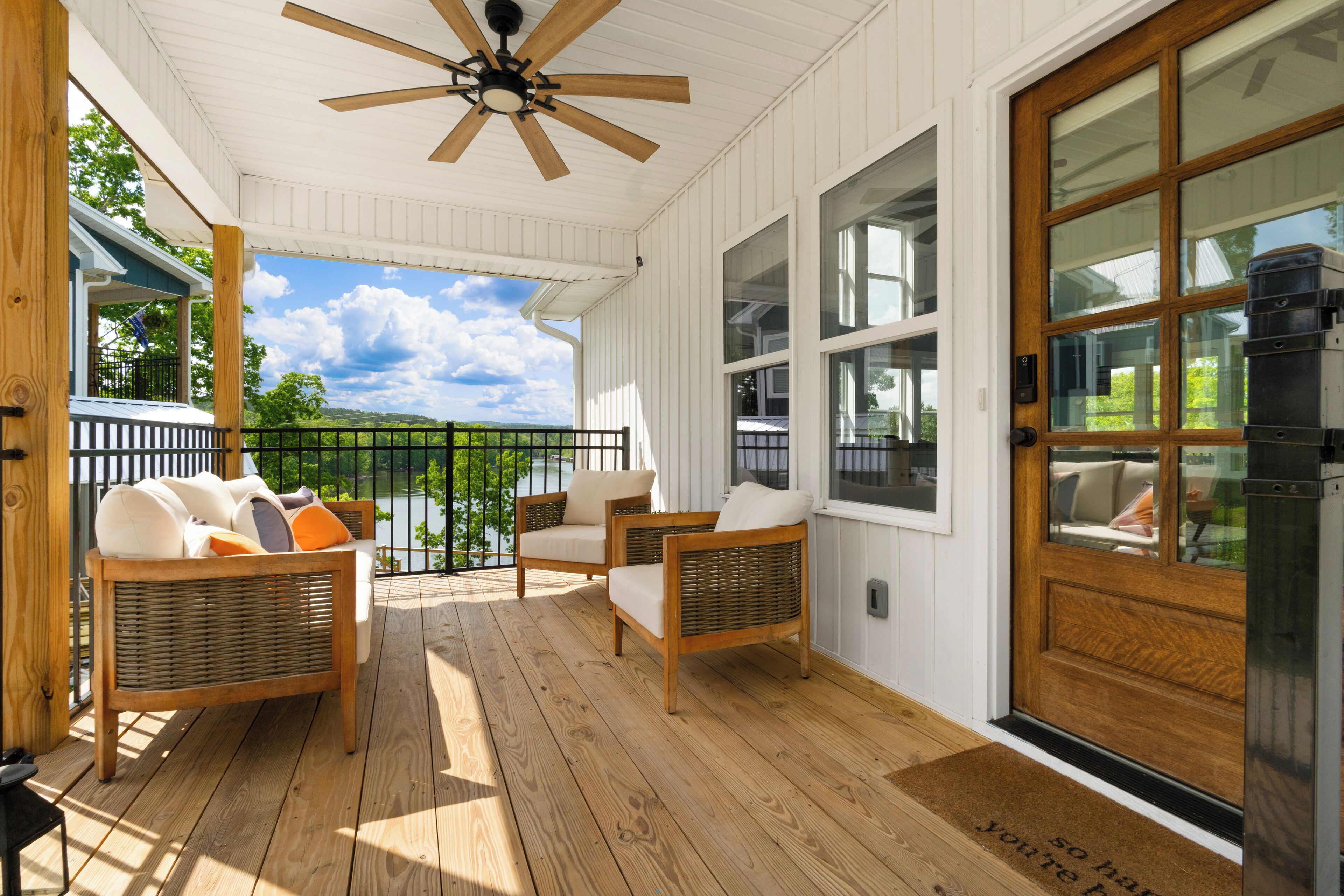 A covered porch with wicker furniture, a wooden door, and a view of a lake.