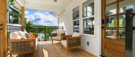 A covered porch with wicker furniture, a wooden door, and a view of a lake.