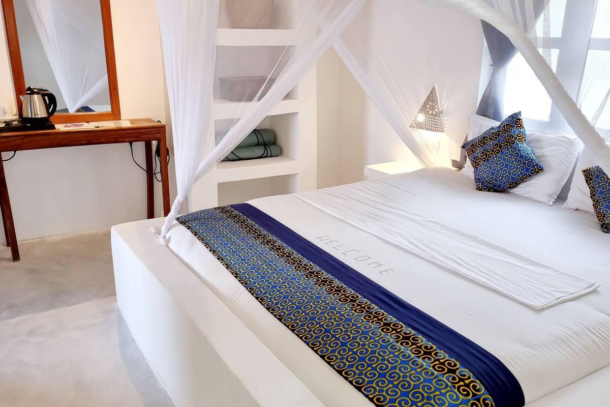A neatly arranged bedroom with a canopy bed, a bedside table, a mirror, and built-in shelving.
