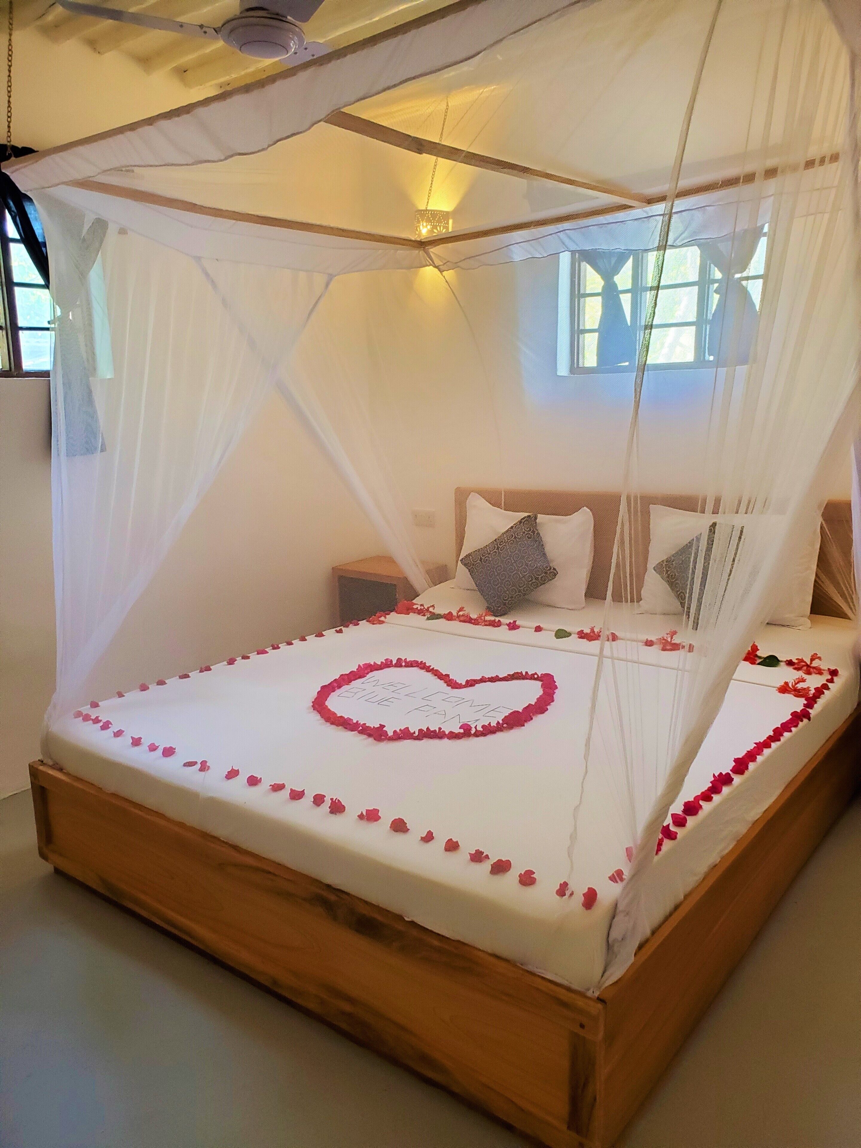 A bed with a canopy, a heart-shaped decoration on the bedspread, and a bedside table with a lamp.