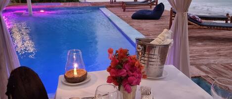 A dining table set for two with a view of the ocean and a pool.