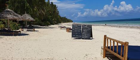 A beach with a wooden bench, a thatched umbrella, and a signboard.