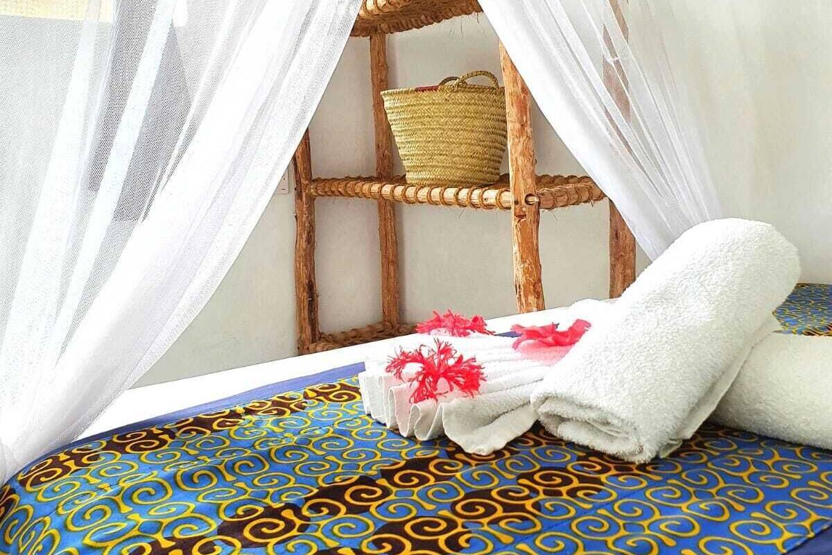 A bed with a blue and yellow patterned bedspread, white towels, and a woven basket on a wooden shelf.