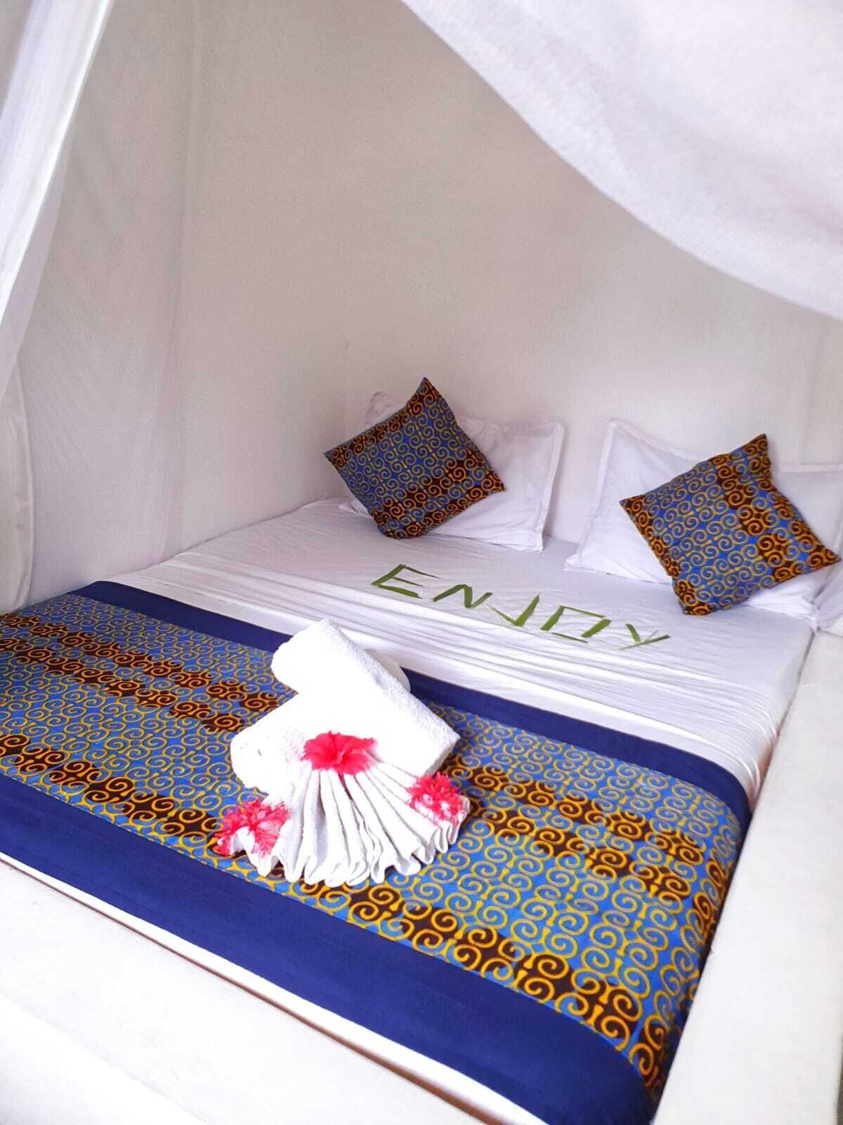 A neatly made bed with a canopy, adorned with a blue and gold patterned bedspread, white pillows, and a decorative towel with pink flowers.