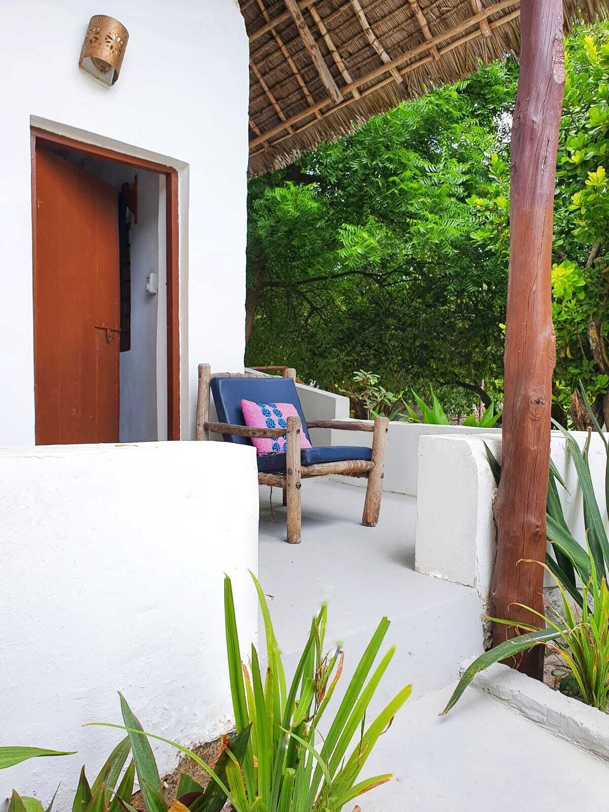 Une chaise en bois avec un coussin, une porte et une structure de toit en chaume.