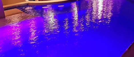 Una piscina con borde curvo y un área de estar cubierta con mesas y sillas.