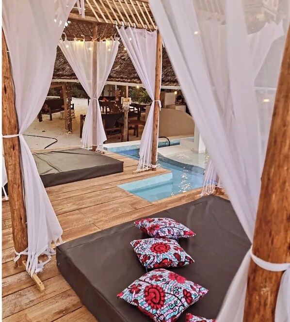 A poolside area with a wooden deck, a small pool, and a canopy with white curtains. - Blue Palm Zanzibar (Bwejuu)