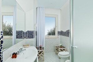 Een moderne badkamer met een grote spiegel, een badkuip, een toilet en een klein tafeltje met een plantje.