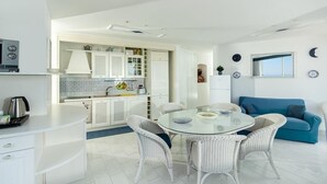 Una cocina moderna con armarios blancos, una mesa redonda de vidrio y un sofá azul en un espacio habitable luminoso.