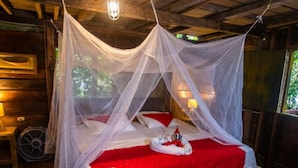 A bed with a red bedspread and white pillows, a bedside table with a lamp, and a canopy over the bed. - Morro Terco Hotel (Nuquí)