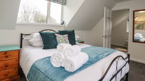 A bedroom with a bed, a window with a floral valance, a wooden nightstand, and a mirror on the wall.