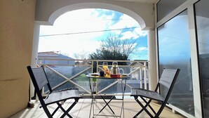 Un balcone con due sedie, un tavolo con un bicchiere e vista su una casa e degli alberi.