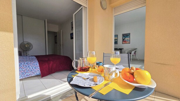 Un balcone con un tavolo apparecchiato per la colazione, che include succo d'arancia, un piatto di frutta e una caffettiera.