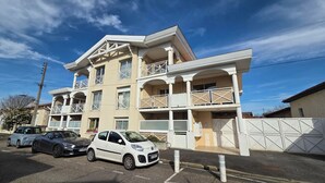 Un edificio a più piani con balconi, un'area di parcheggio con auto e un cielo sereno.