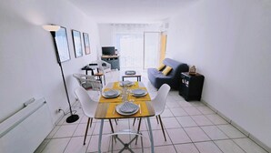 Zona pranzo con tavolo imbandito per quattro persone, sedie, divano, televisore e un piccolo mobiletto.