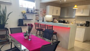 A modern kitchen with a central island, a dining area with a glass table and chairs, and a potted plant. - Cancun Joyful (Cancun)