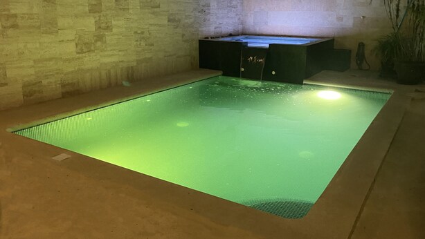 A rectangular indoor swimming pool with a greenish tint, surrounded by a stone wall and a black cabinet with drawers. - Cancun Joyful (Cancun)
