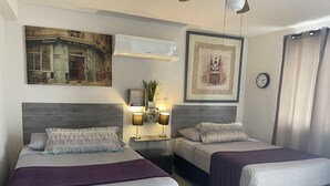 A hotel room with two beds, a nightstand with lamps, a wall-mounted air conditioner, and framed artwork. - Cancun Joyful (Cancun)