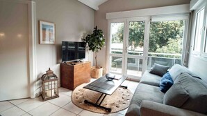 A living room with a sofa, a TV, a plant, and a wooden cabinet. - Cozy apartment by the sea (La Teste-de-Buch)