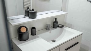 A modern bathroom with a white sink, black and gray fixtures, and a mirror above the countertop. - Cozy apartment by the sea (La Teste-de-Buch)