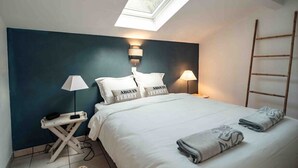 A bedroom with a skylight, a bed with white bedding, two bedside lamps, and a wooden ladder against the wall. - Cozy apartment by the sea (La Teste-de-Buch)