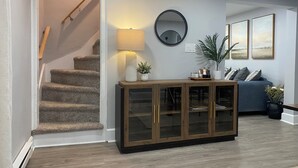 A staircase leading to a second floor, a round mirror on the wall, a wooden cabinet with glass doors, and a blue sofa with cushions. - Lakefront on Main  (Elmer)