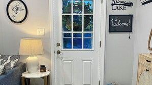 A room with a white door, a lamp, a framed picture, and a welcome sign. - Lakefront on Main  (Elmer)