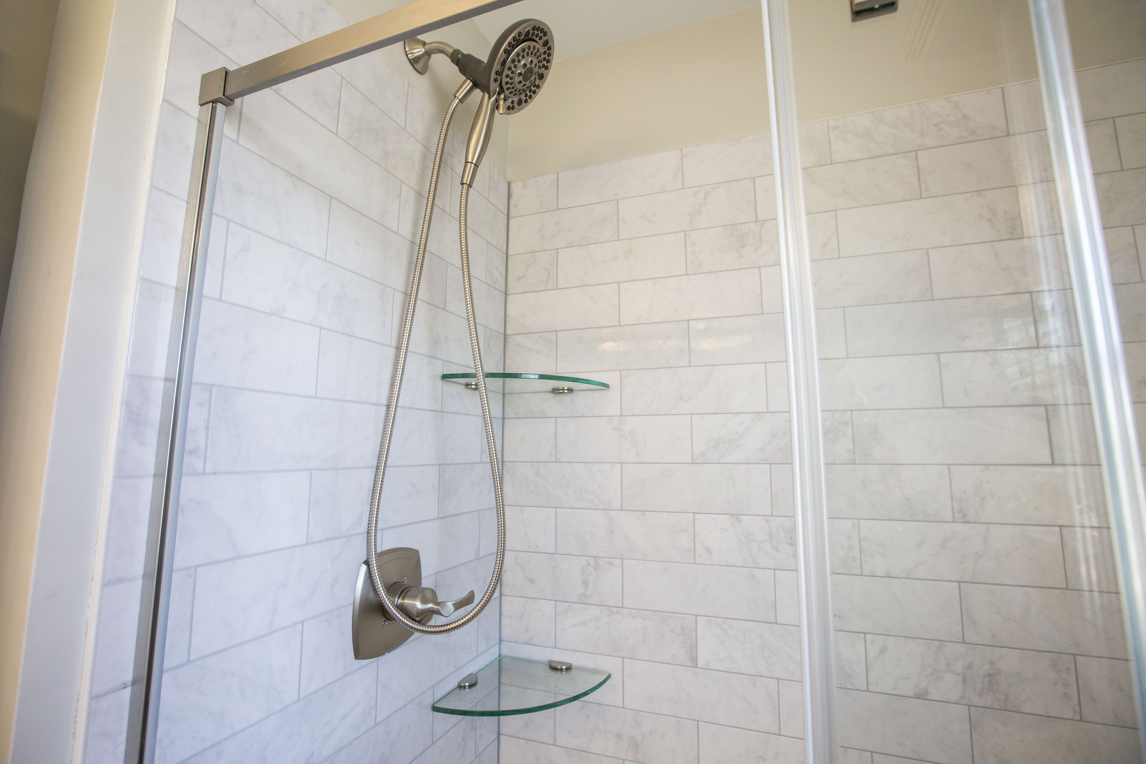 Ducha envuelta en vidrio con cabezal de ducha de mano y repisa de vidrio.