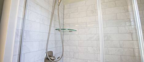 Ducha envuelta en vidrio con cabezal de ducha de mano y repisa de vidrio.