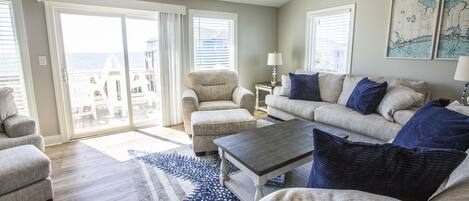 A spacious living room with a large sliding glass door leading to a balcony, a sofa set, a coffee table, and a rug.
