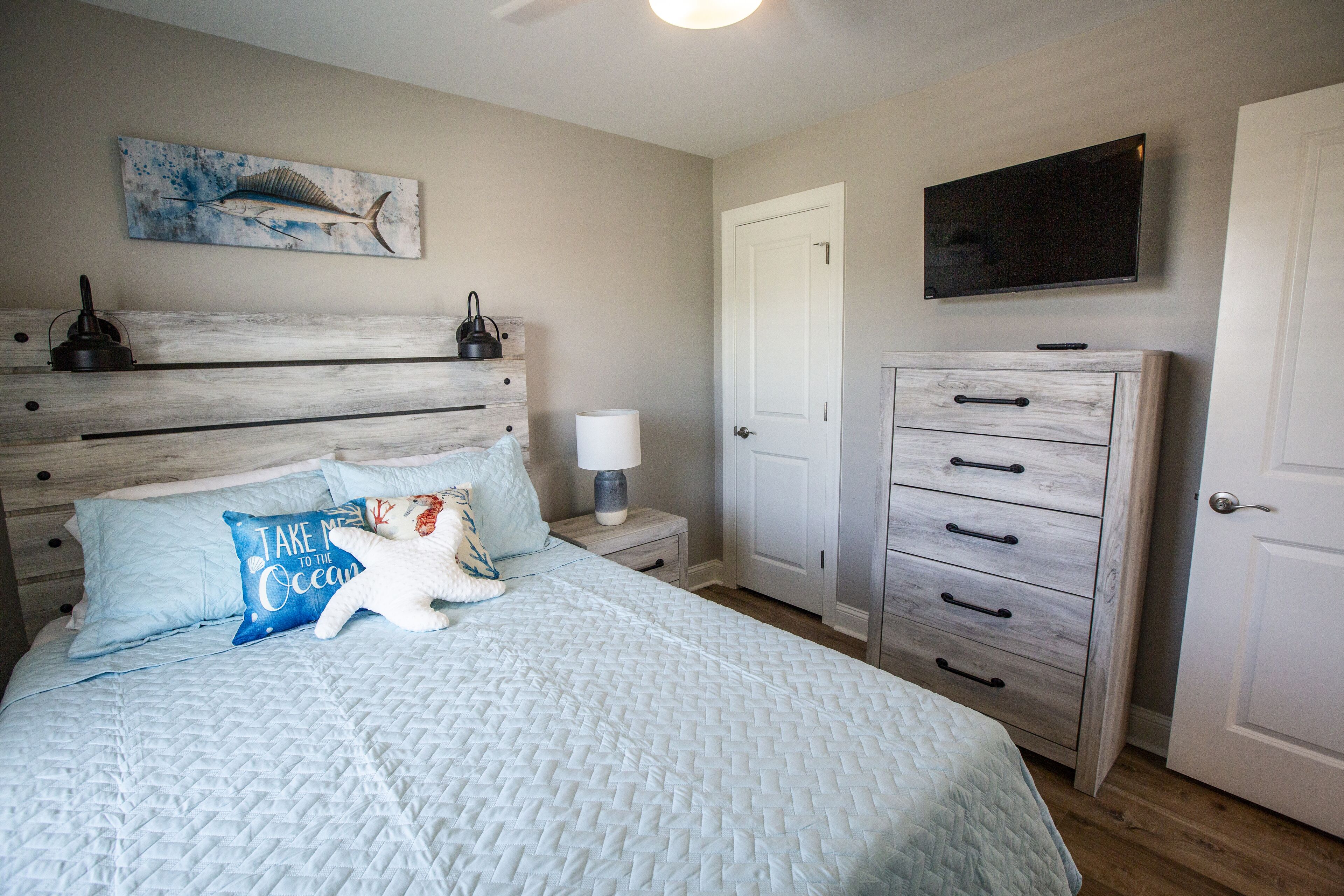 A bedroom with a bed, a dresser, a nightstand, a lamp, a television, and a wall-mounted artwork.