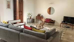 Una sala de estar con un sofá gris, una mecedora de madera, una mesita y un mueble de televisión con un televisor de pantalla plana.