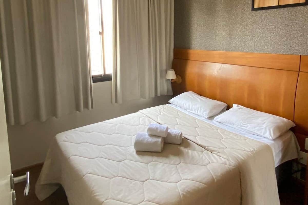 Une chambre d’hôtel avec un grand lit, une tête de lit en bois, une fenêtre avec des rideaux et une œuvre d’art accrochée au mur.