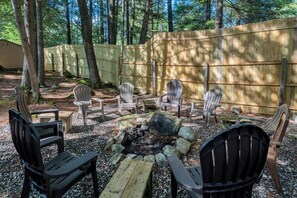 Un espacio al aire libre con sillas Adirondack y un brasero, todo rodeado por una valla de madera.