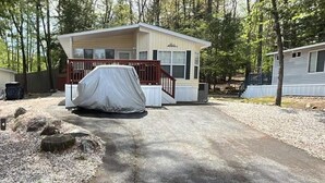 Ein Bungalow mit einem überdachten Stellplatz, umgeben von Bäumen und Kies.