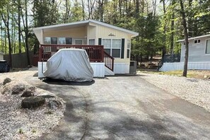 Une maison mobile de plain-pied, avec un abri-voiture couvert à l’avant, entourée d’arbres.