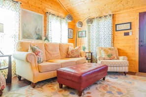 A cozy cabin interior with a beige sofa, a red ottoman, and a patterned armchair. - Cabin 2 at Widows Peak • Terlingua, Big Bend (Terlingua)